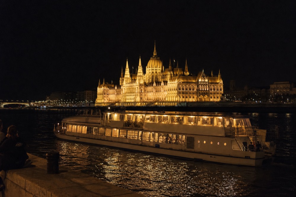 A illuminated dinner cruise boat gliding past the lit Hungarian Parliament on the Danube at night, no text, no logos, no people.