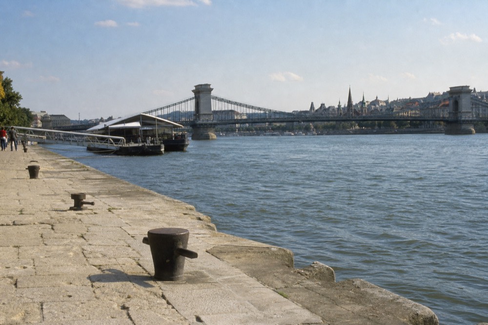 Numbered stone embankment steps and mooring bollards on the Pest side of the Danube with the Chain Bridge behind, no text, no logos, no people