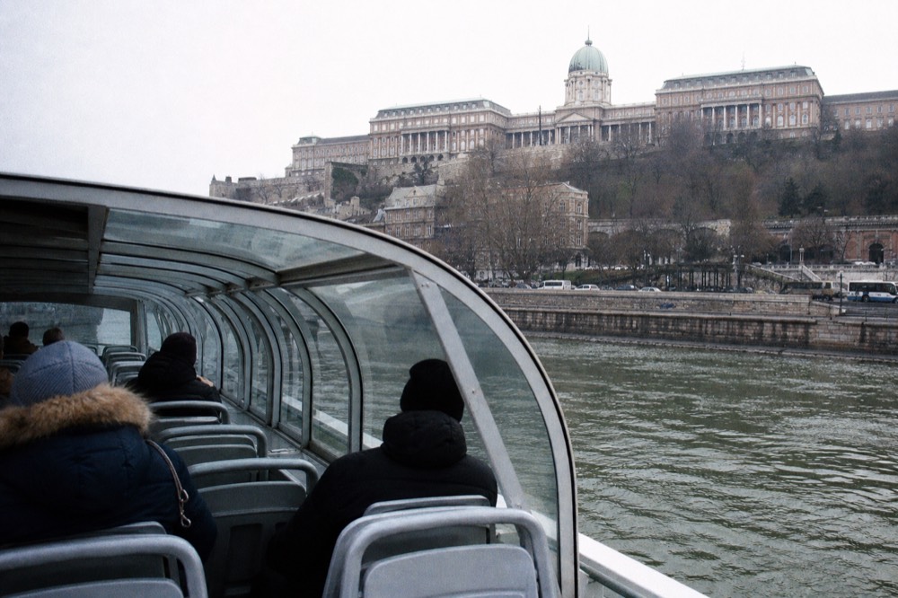 A glass-enclosed sightseeing boat on the Danube in winter, with Buda Castle on the hill above, no text, no logos, no people.