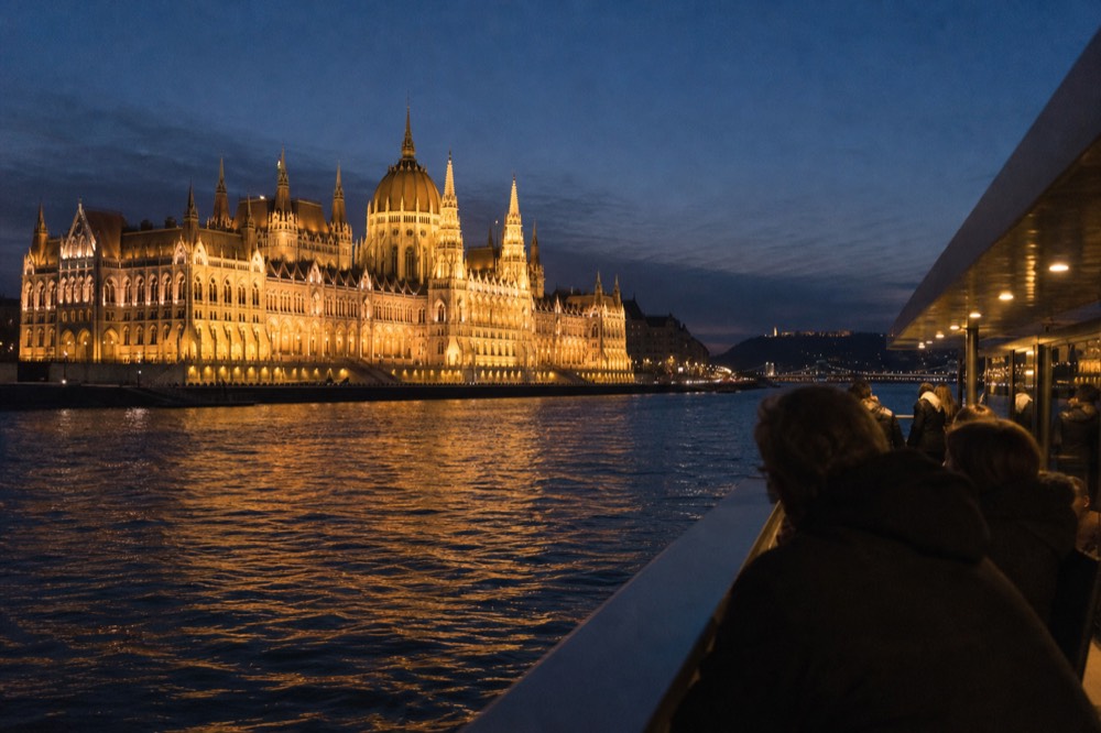 A sightseeing boat on the Danube passing the illuminated Hungarian Parliament at dusk, no text, no logos, no people.