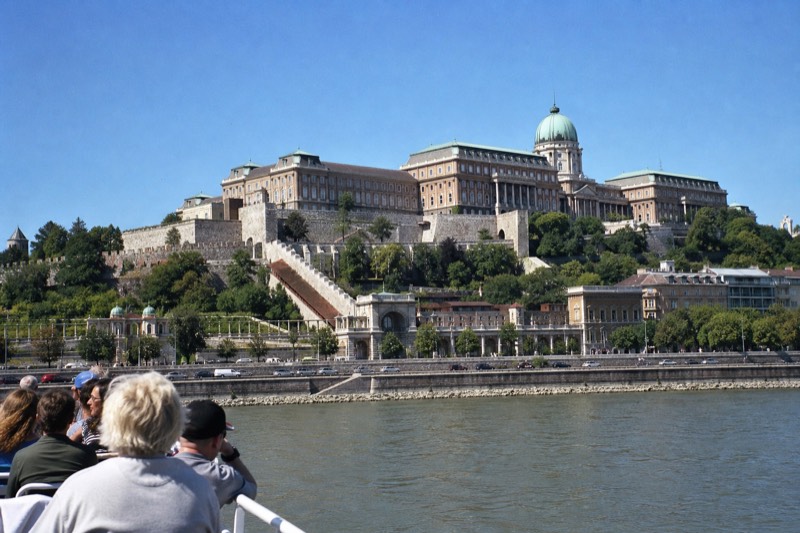 A daytime sightseeing boat on the Danube in bright sunlight with the Buda Castle hillside rising behind it