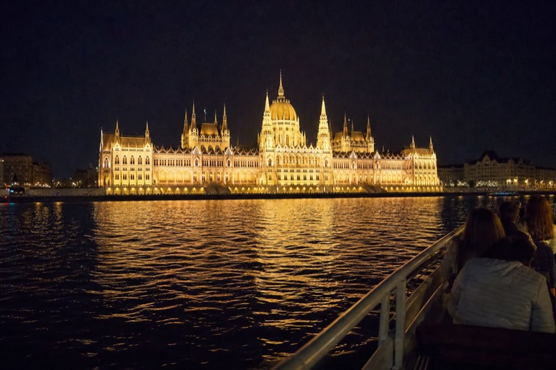 The illuminated Hungarian Parliament building seen from the water at night, its dome and spires reflected in the dark Danube