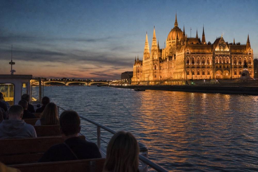 A sightseeing boat cruising the Danube past the illuminated Hungarian Parliament at dusk, no text, no logos, no people.
